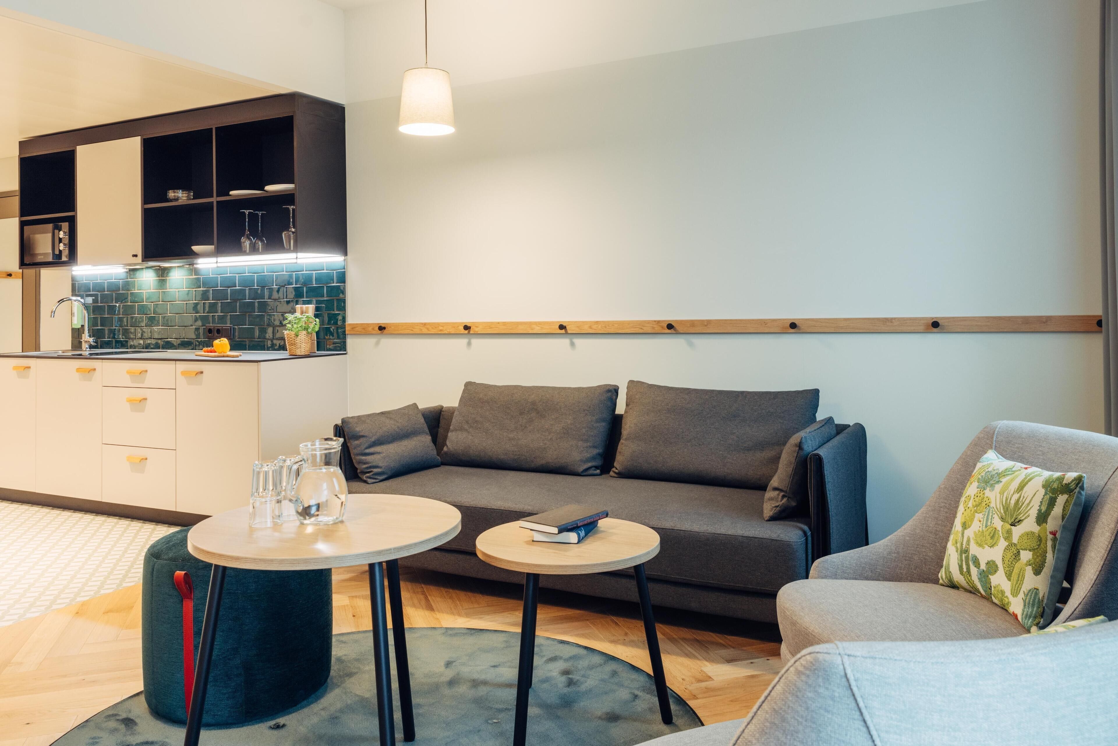 A modern living room with a sofa, two small tables, and a kitchen area with a tiled backsplash.