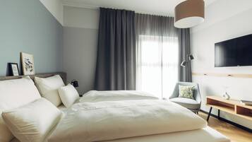 Ein modernes Hotelzimmer mit einem großen Bett, einem Schreibtisch, einem Stuhl, einem Fernseher und einem Fenster mit Vorhängen.