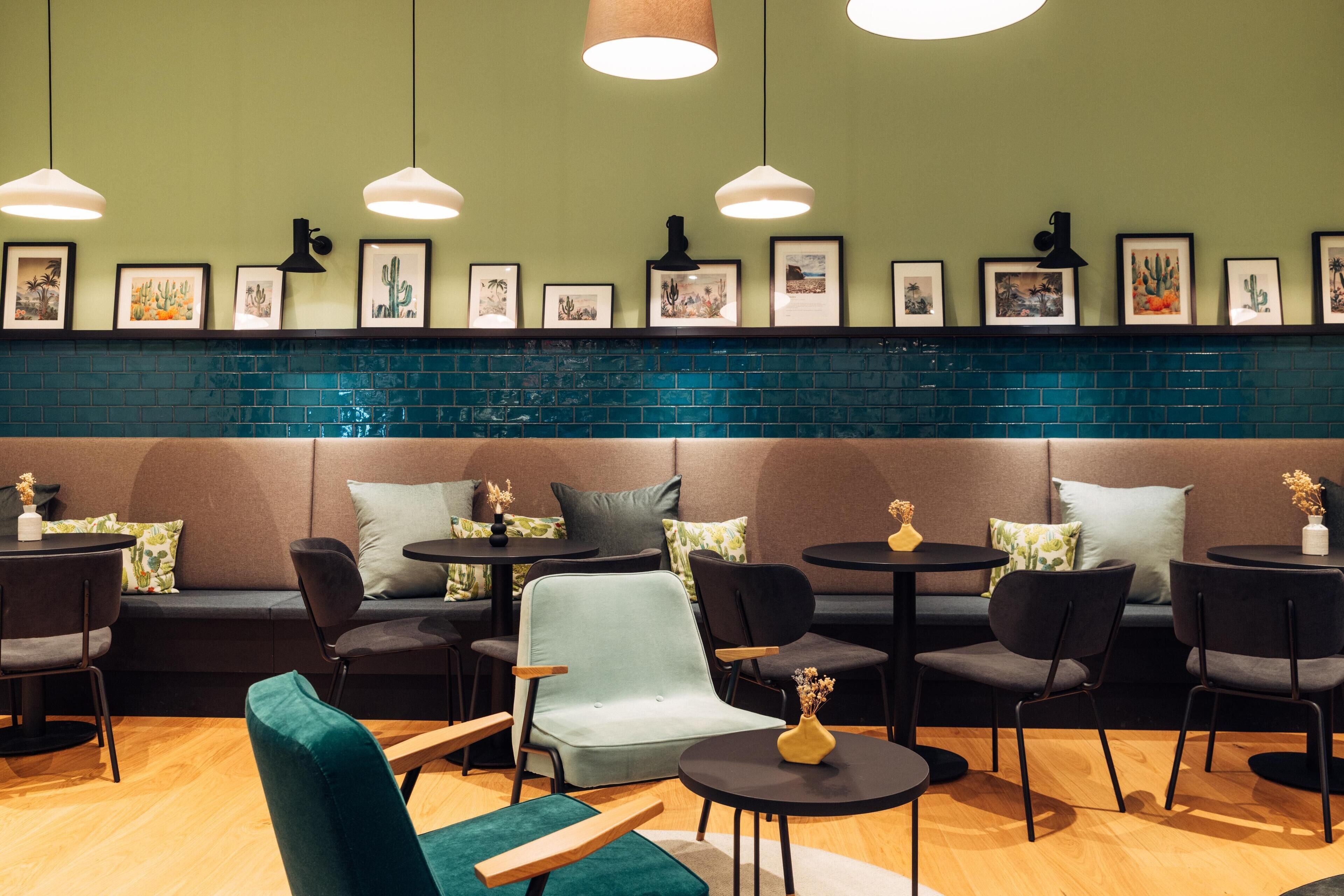 A cozy cafe with a green wall, blue-tiled backsplash, and a variety of seating options including sofas and chairs.