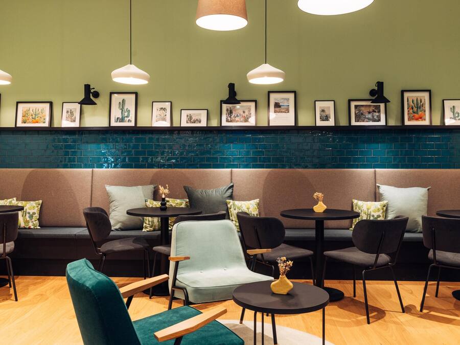 A cozy cafe with a green wall, blue-tiled backsplash, and a variety of seating options including sofas and chairs.