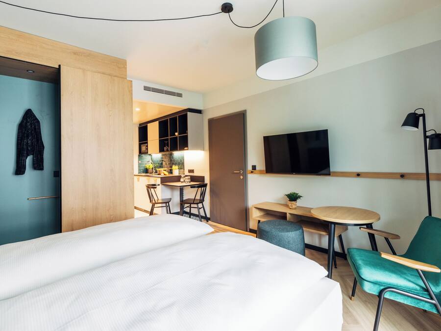 Una habitación de hotel moderna con una cama, un escritorio, una silla, un televisor y un rincón de comedor.