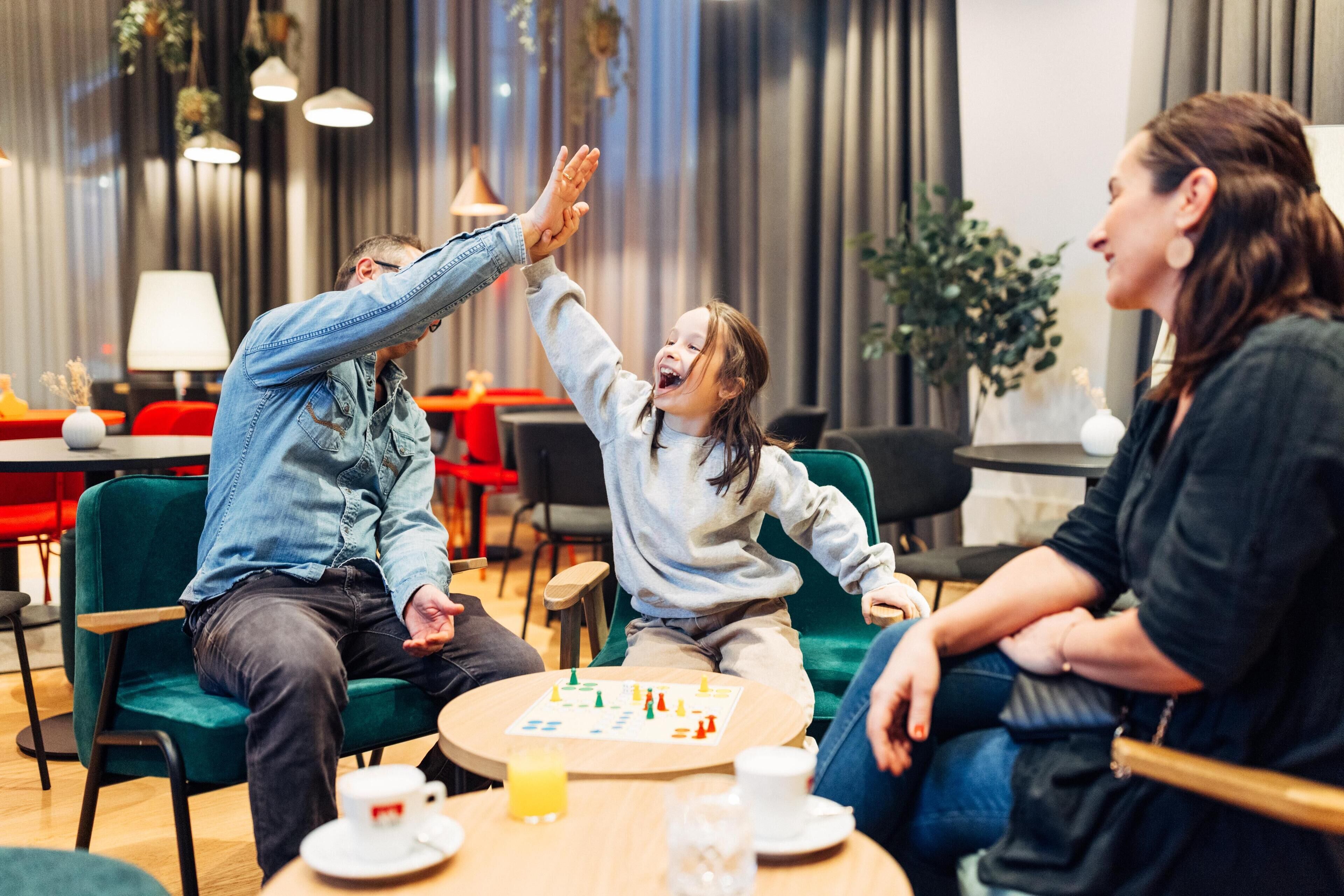 A group of people sitting around a table in a modern indoor setting with chairs and a table with a board game.