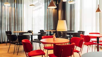 A modern dining area with round tables and red chairs, featuring pendant lighting and a large window with curtains.