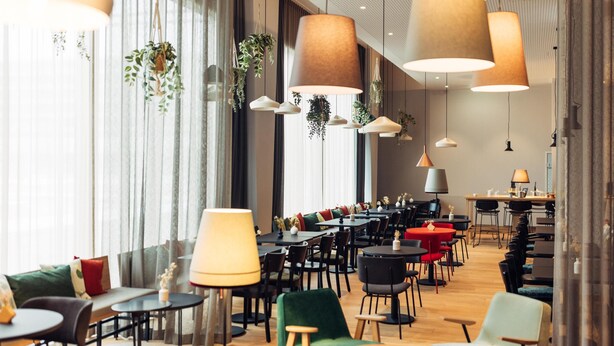 Un comedor moderno con varias mesas y sillas, plantas colgantes e iluminación colgante grande.