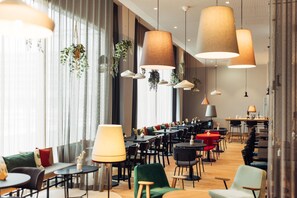 Een moderne eetruimte met meerdere tafels en stoelen, hangplanten en grote hanglampen.