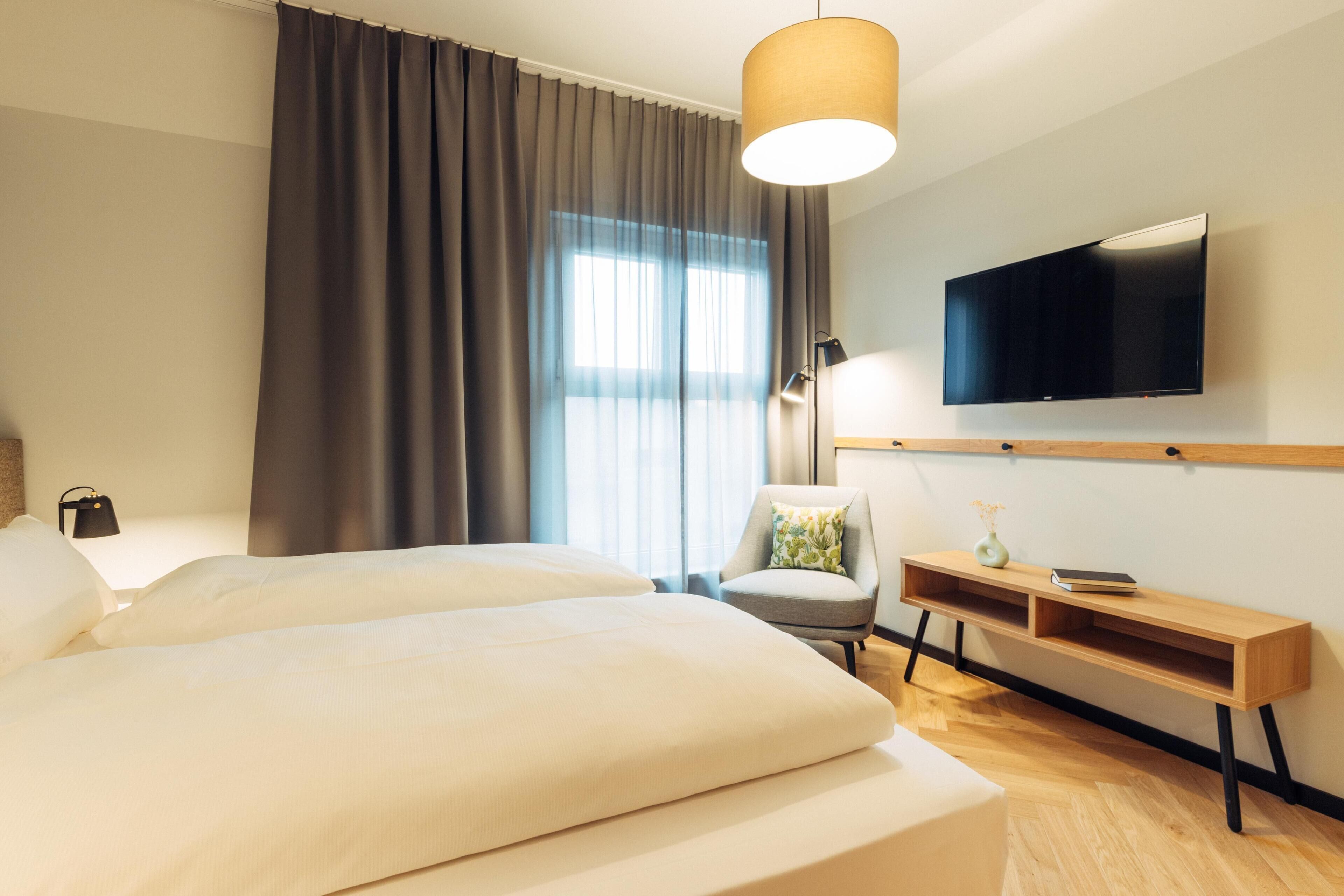 A hotel room with two beds, a TV, a desk, and a chair.