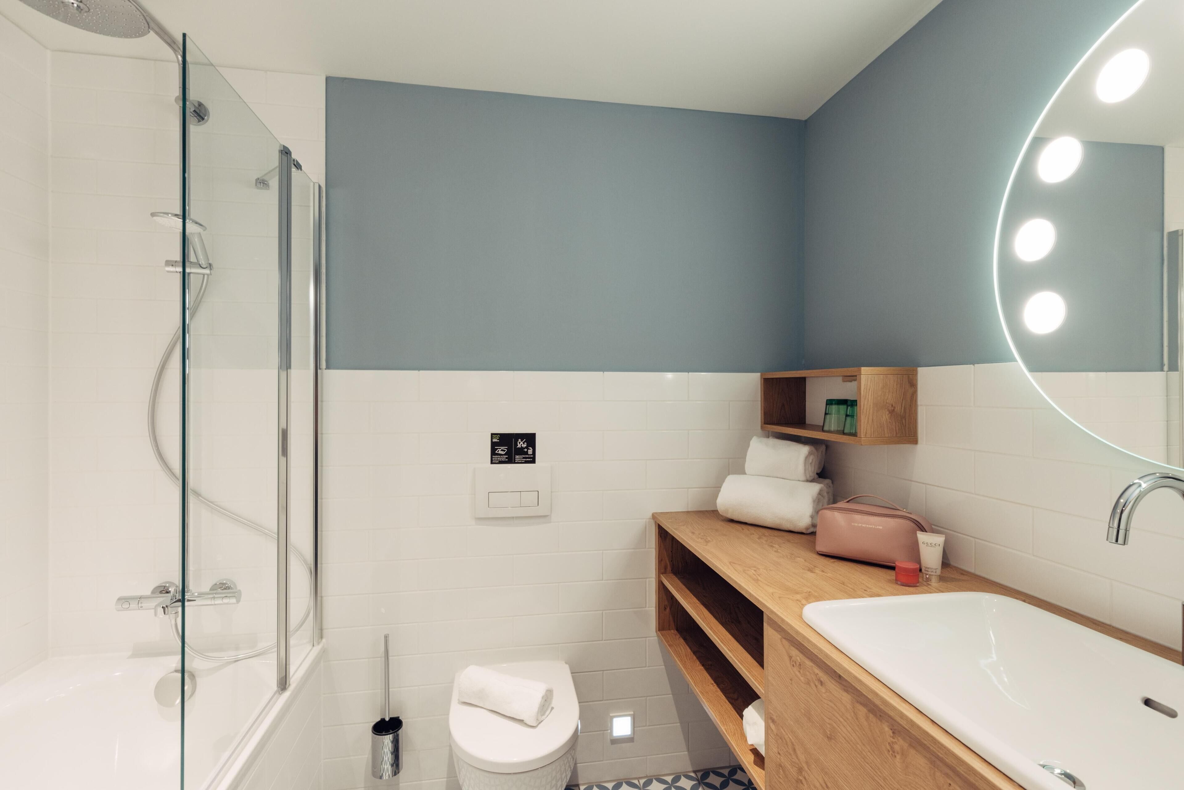 A modern bathroom with a glass shower enclosure, a white toilet, a wooden vanity with a sink, and a mirror with lights.
