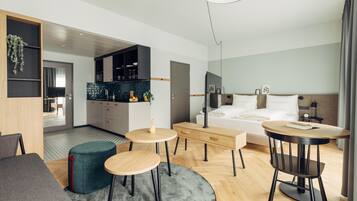 Una habitación de hotel moderna con cama, escritorio, mesa de comedor y kitchenette.