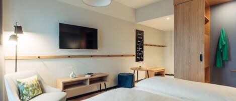 Una habitación de hotel moderna con una cama grande, un televisor de pantalla plana montado en la pared, un escritorio pequeño y una silla con cojín.