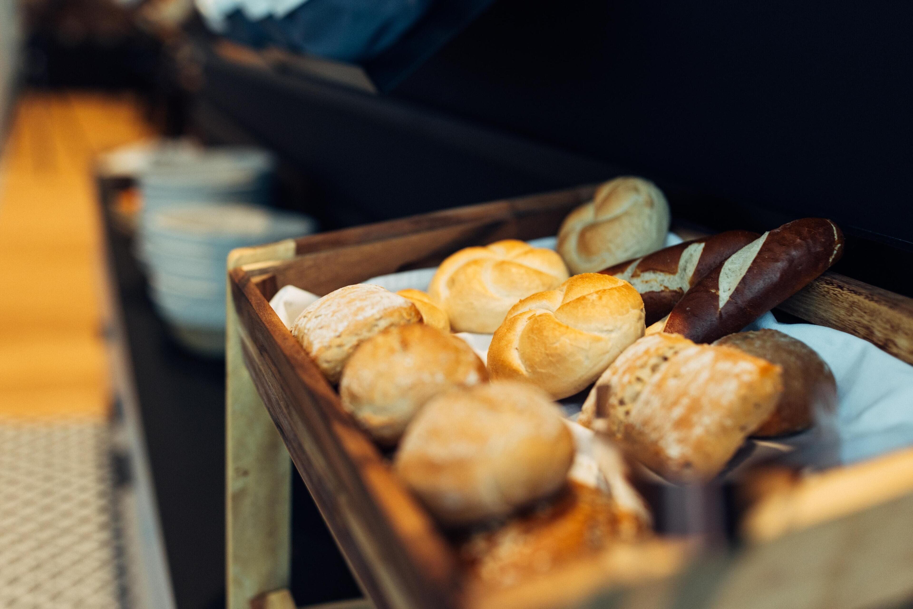 A tray of assorted baked goods, including rolls and baguettes, on a wooden table.