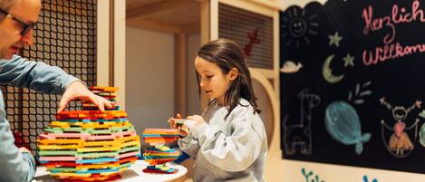 A child playing with colorful building blocks at a table, with a chalkboard in the background displaying drawings and text.