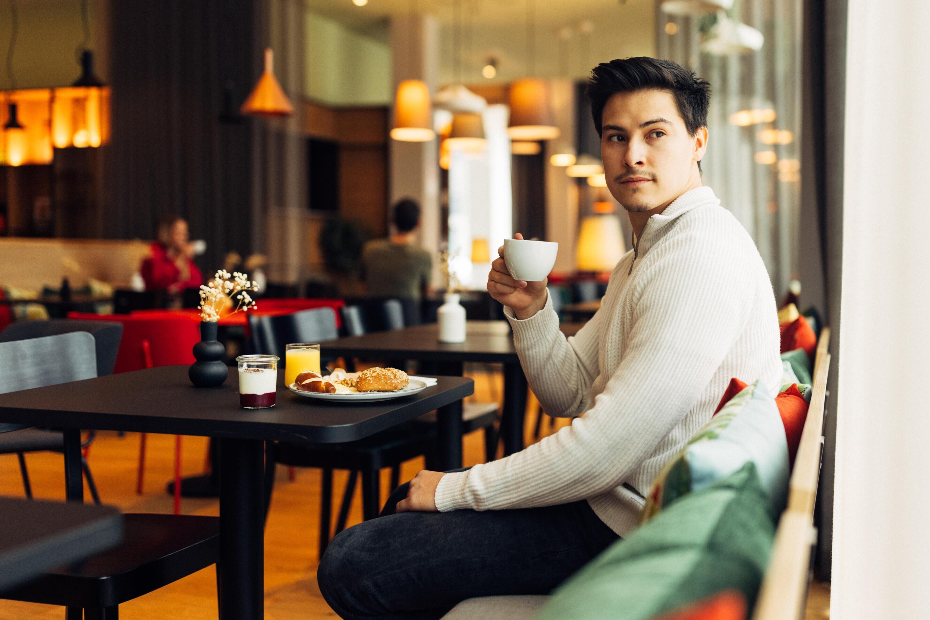 A person sitting at a table in a modern cafe with a cup and a plate of food.