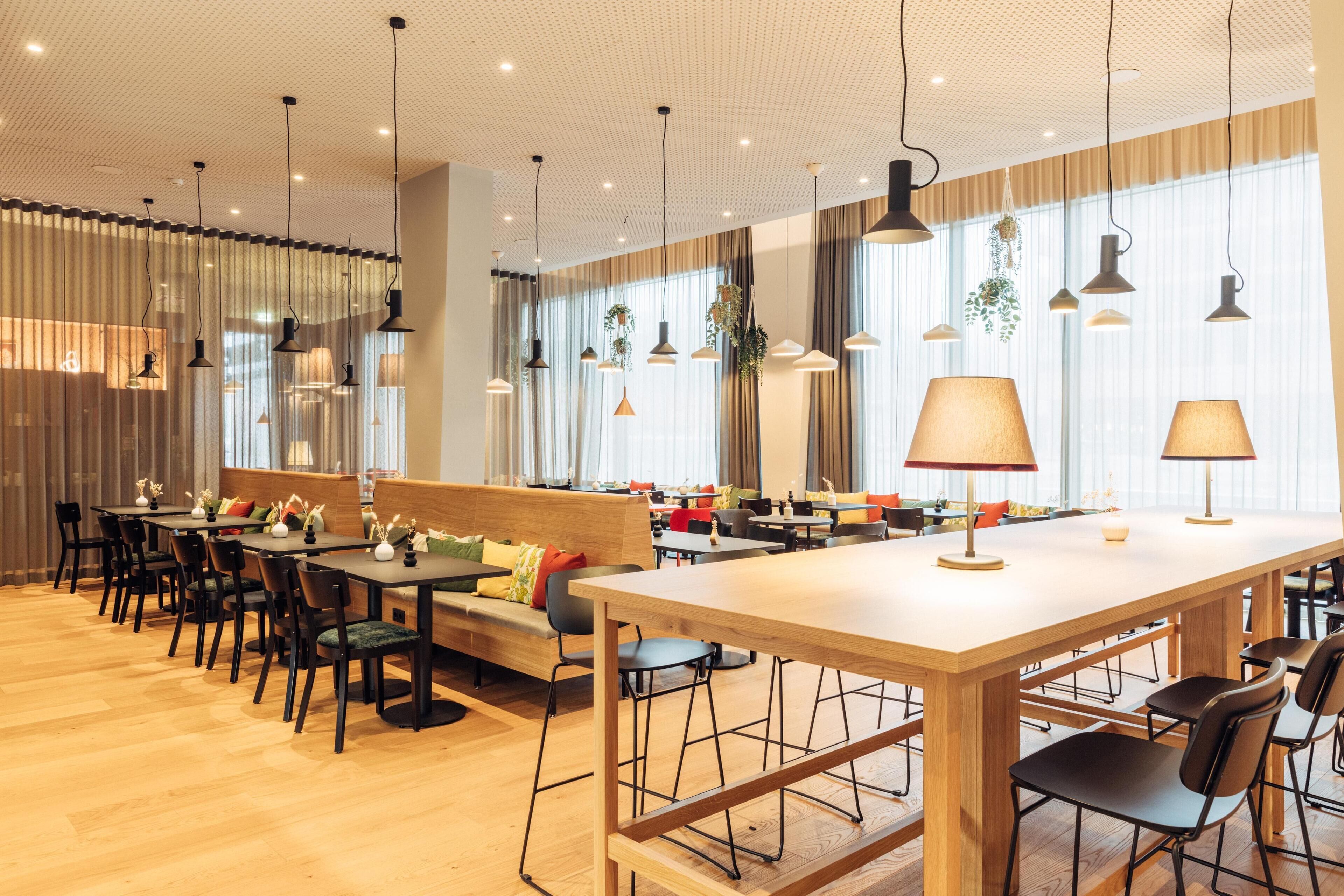 A modern restaurant with wooden tables, black chairs, and a central bar area.