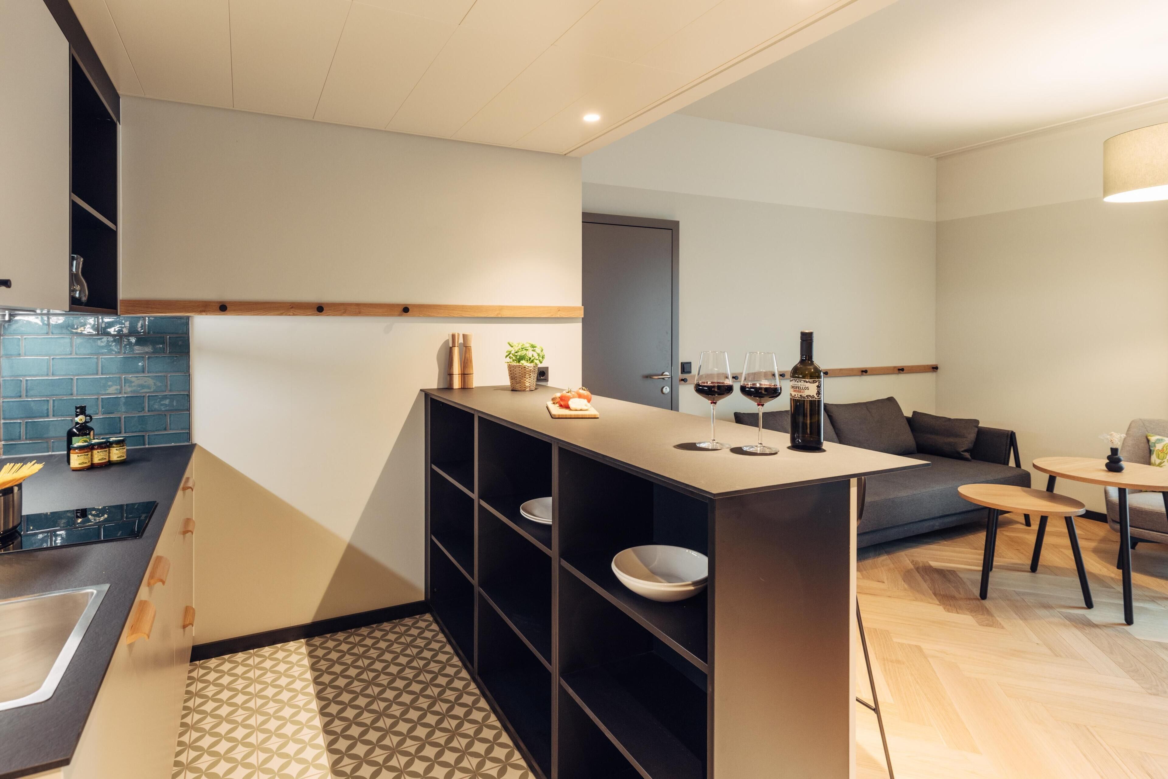 A modern kitchen with a built-in island, black shelving, and a dining area with a sofa and a small table.
