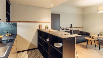 Una cocina moderna con una isla integrada, estanterías negras y una zona de comedor con sofá y una mesa pequeña.