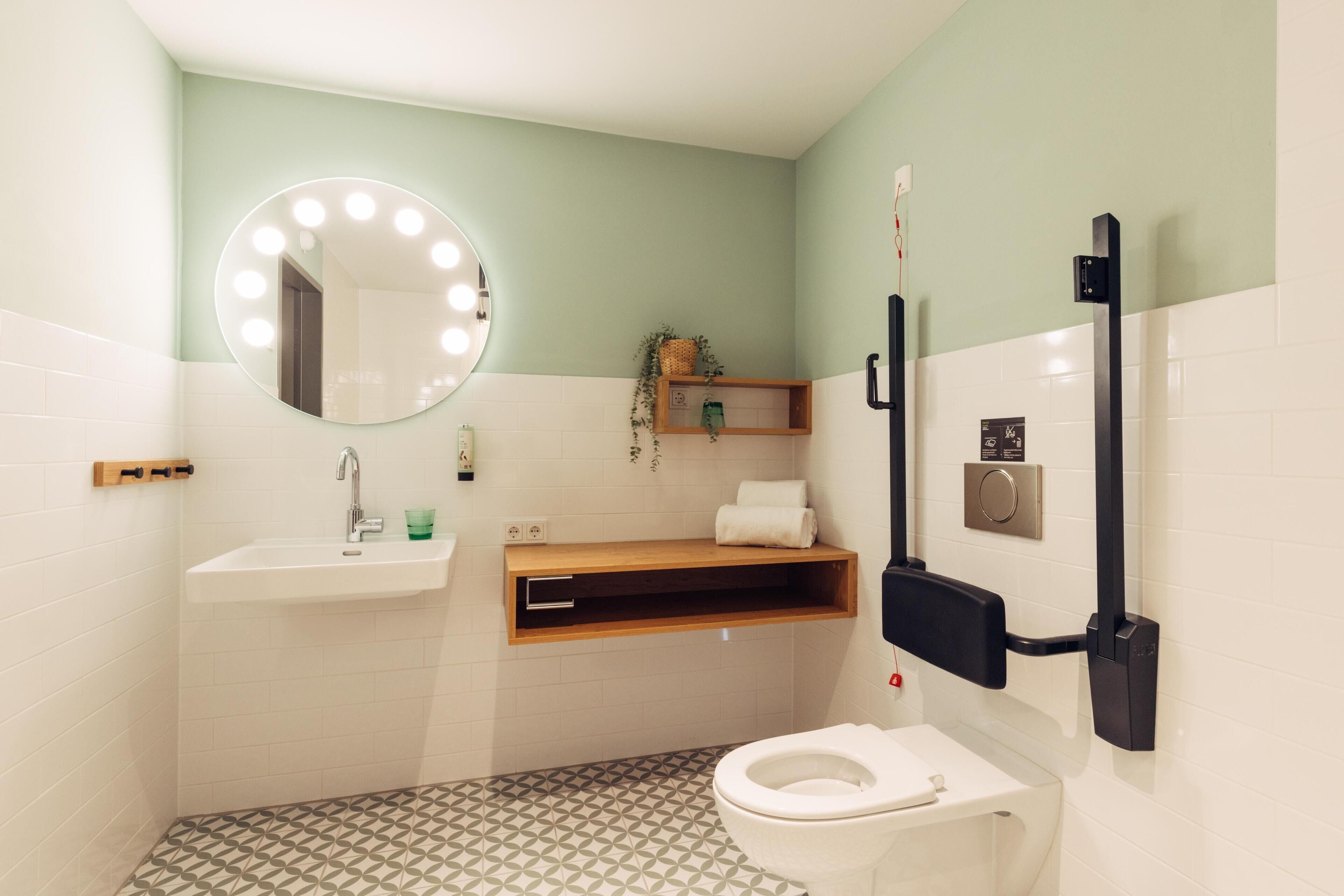 A bathroom with a white sink, a mirror with lights, a toilet, and a shelf with a plant.