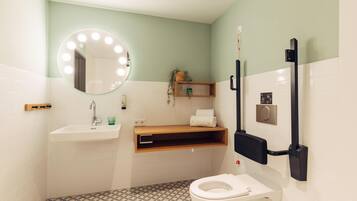 A bathroom with a white sink, a mirror with lights, a toilet, and a shelf with a plant.