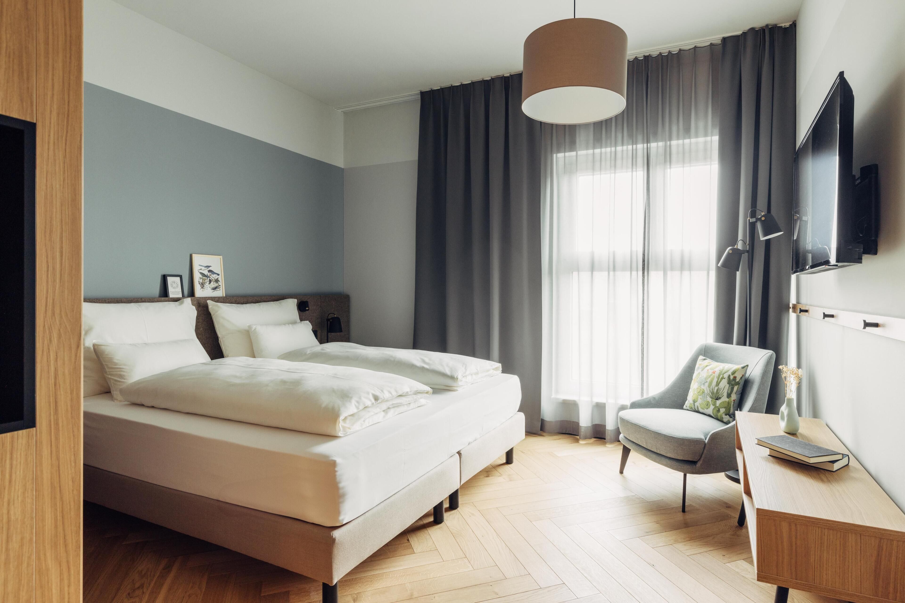 A modern bedroom with a bed, a desk, a chair, and a TV.