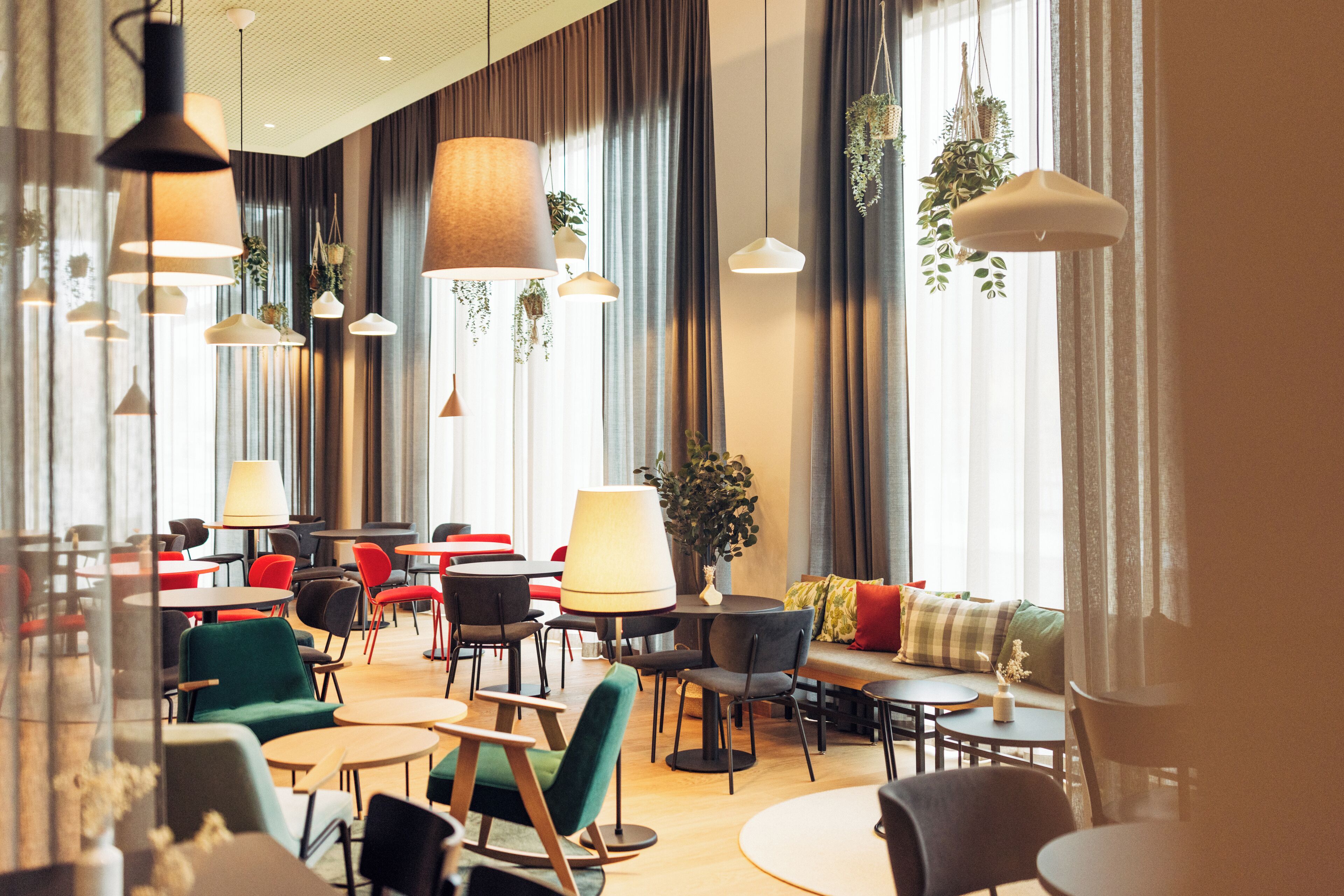 A modern hotel lobby with multiple seating areas, including round tables and chairs, and a sofa with cushions.