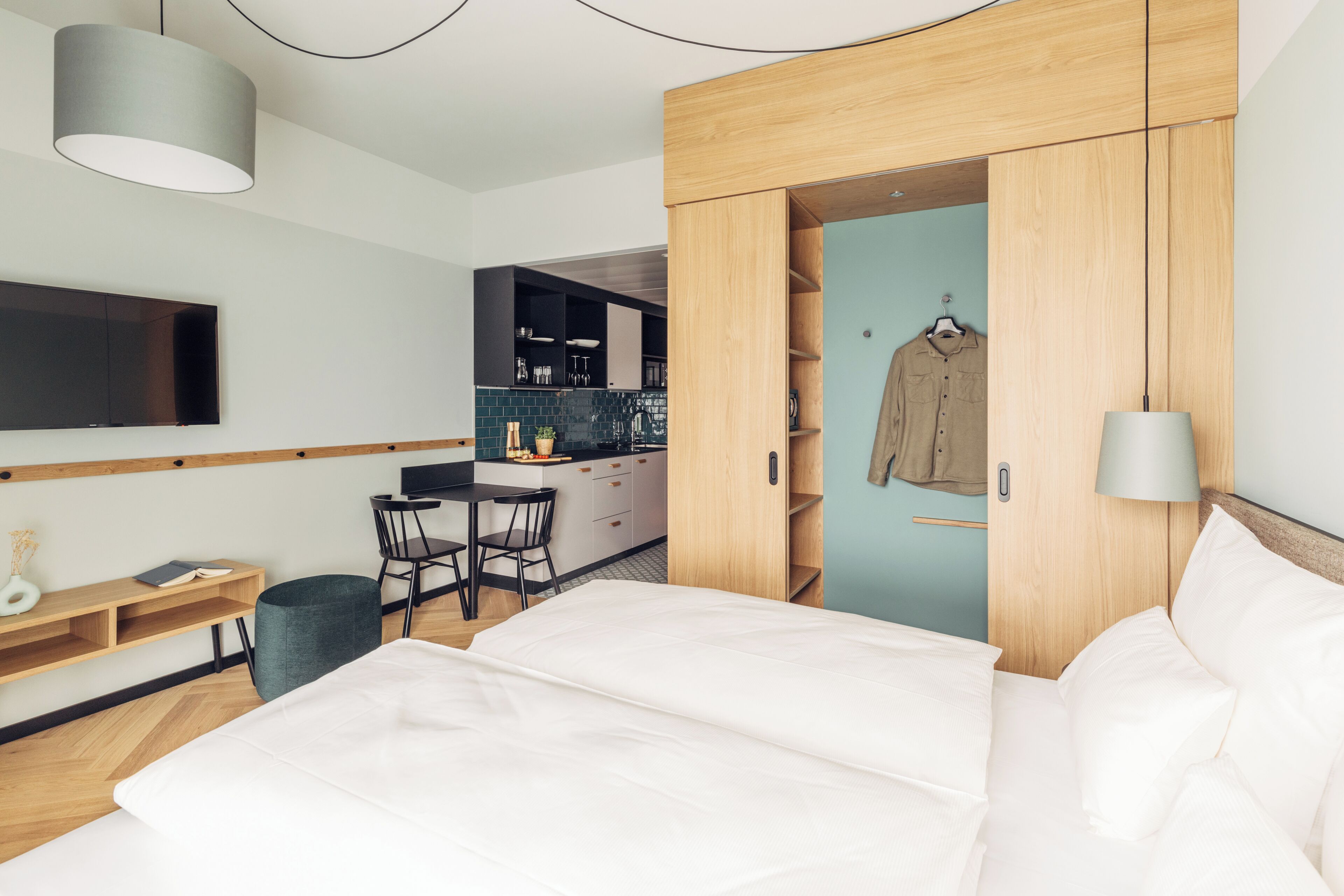 Una habitación de hotel moderna con cama, escritorio, silla, televisor y kitchenette.