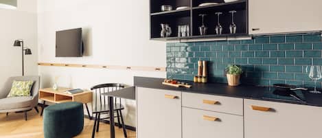 A modern kitchen with a black countertop, white cabinets, and a teal backsplash. There is a dining area with a wooden table and chairs, and a green ottoman.