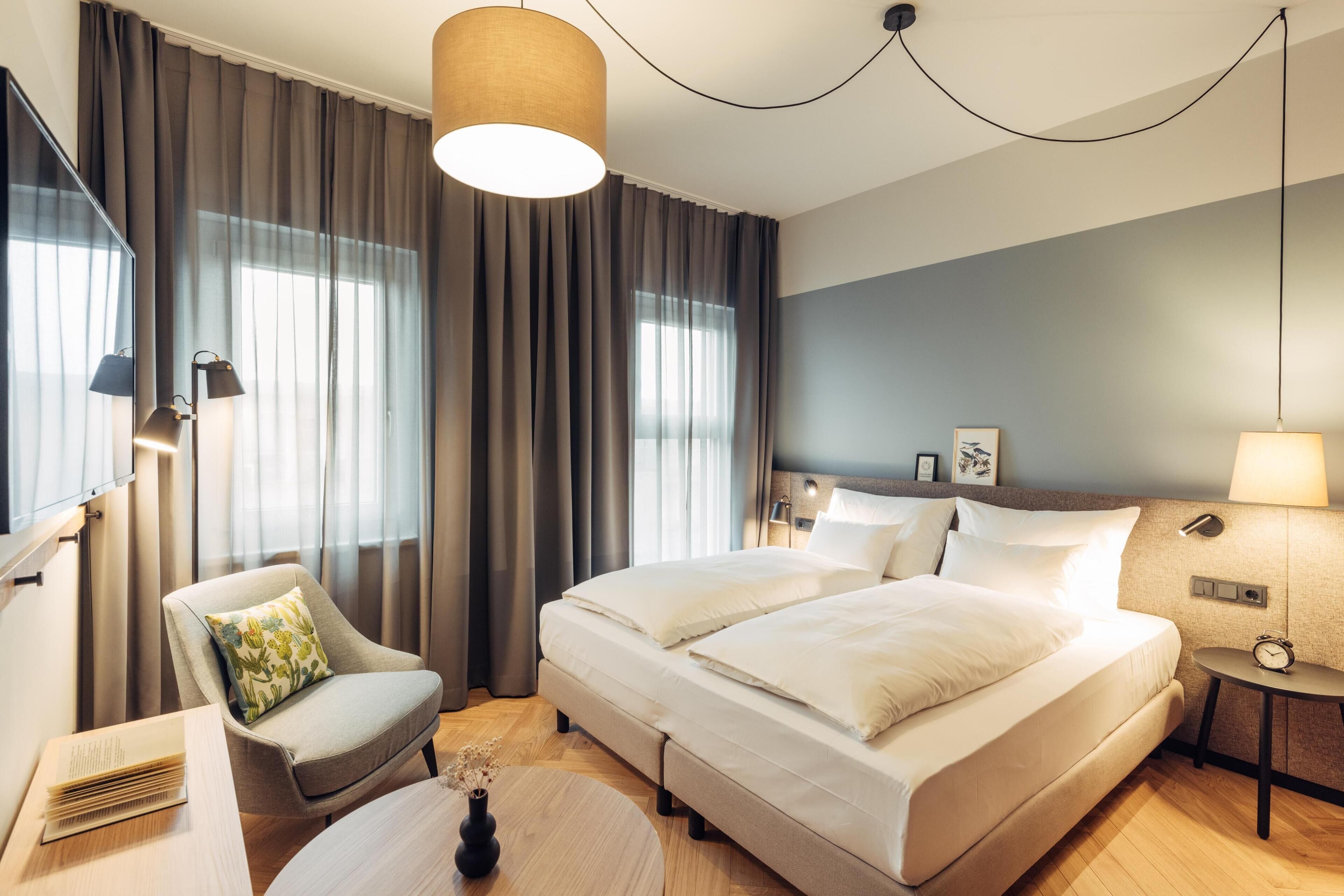 Ein Hotelzimmer mit einem großen Bett, einem Sessel, einem Schreibtisch, einer Lampe und einem Nachttisch.