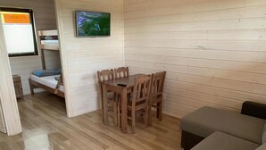 Una stanza accogliente con pavimento in legno, un letto a castello, un tavolo da pranzo con sedie e un televisore montato a parete.