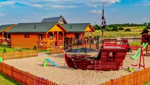 A wooden cabin with a green roof, a small boat-shaped play structure, and a slide. - Cozy Holiday Houses Near the Sea, Sarbinowo (Mielno)