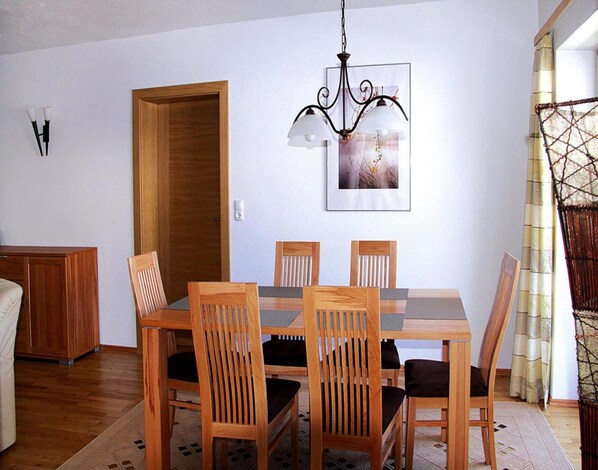 A dining area with a wooden table and chairs, a chandelier, a framed picture on the wall, and a wooden door. - Apartment in Kitzbuhel Alps With Wellness Area (Wildschönau)