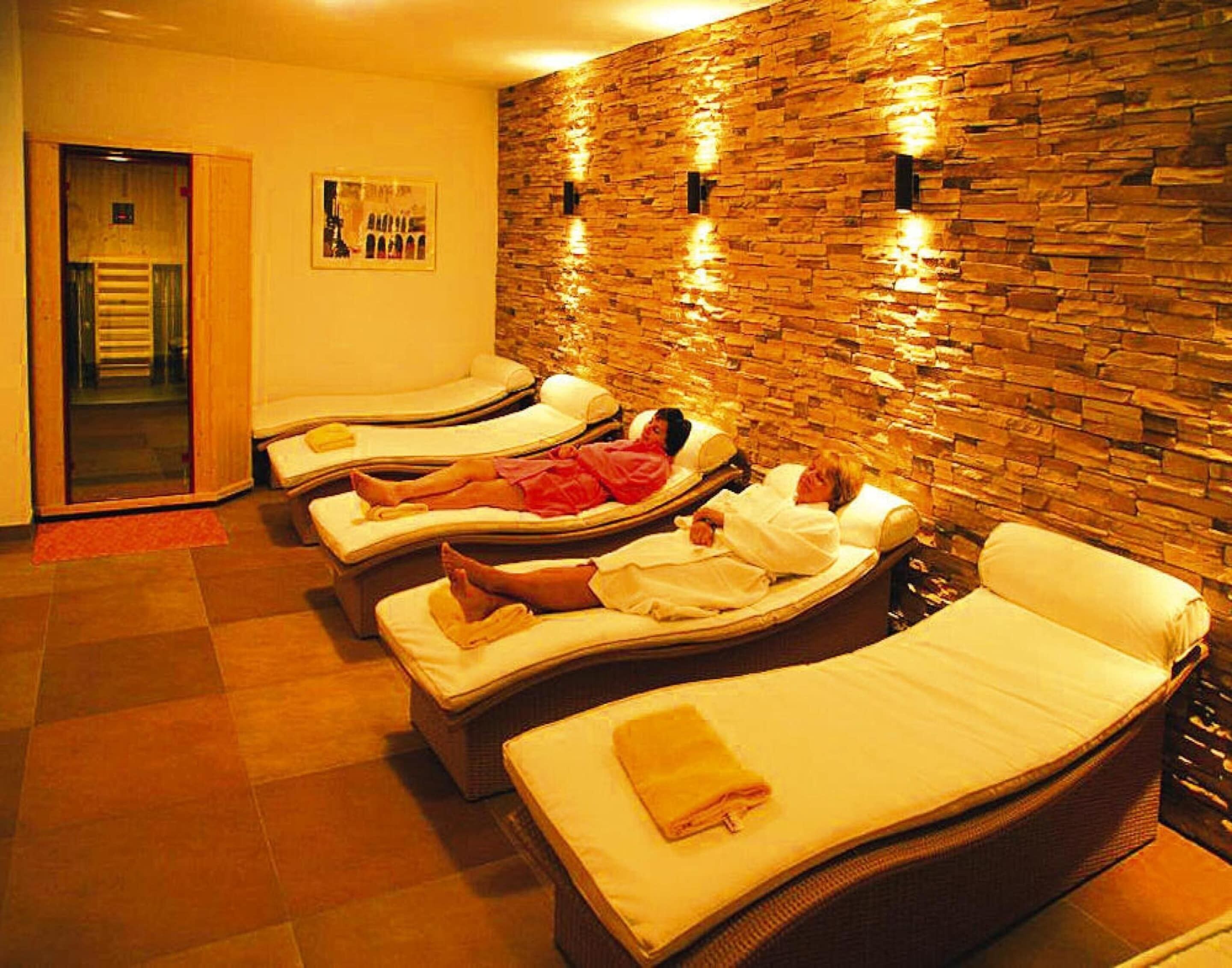 A room with four reclining massage chairs arranged in a row against a stone wall.