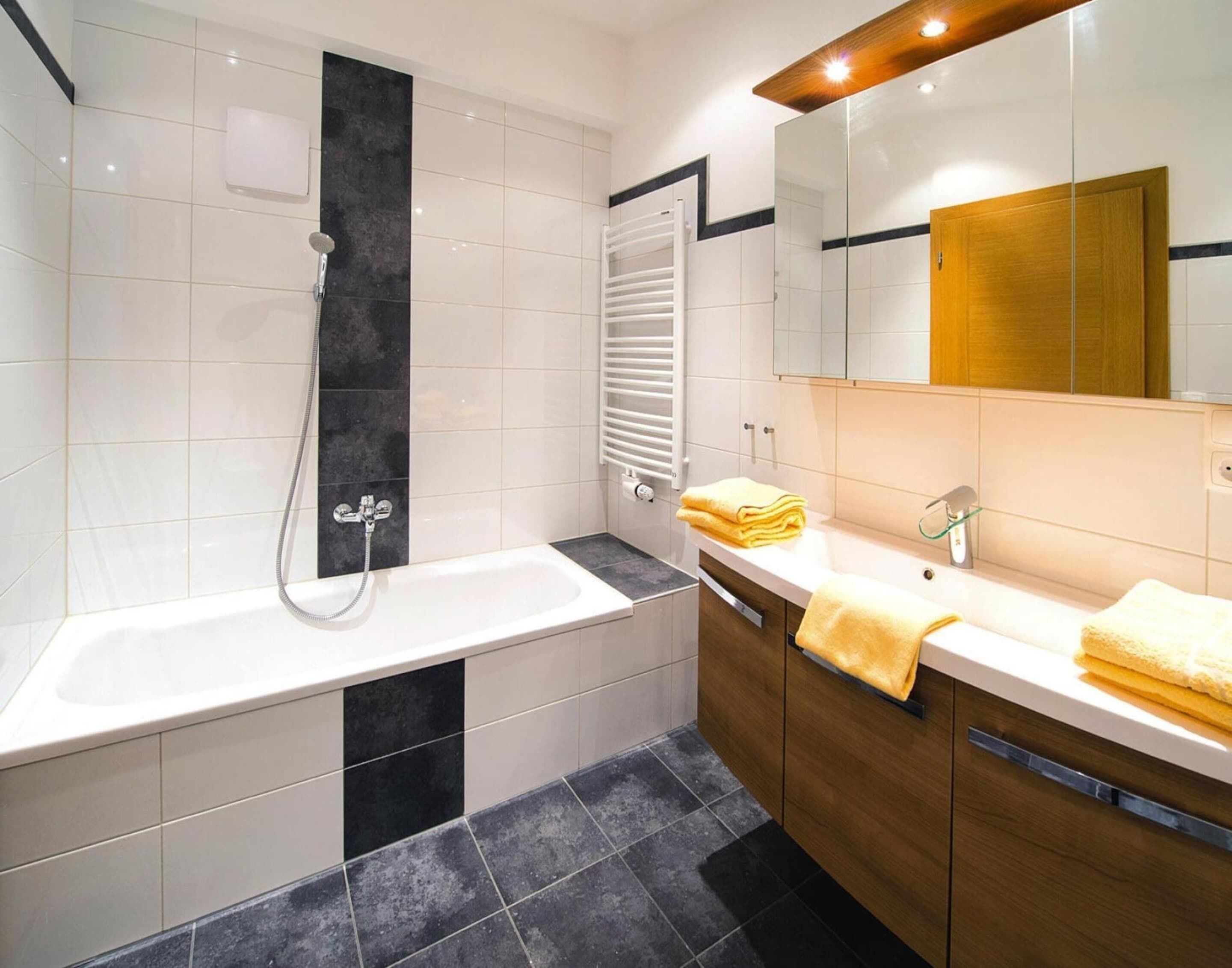 A modern bathroom with a bathtub, a shower, a vanity with a mirror, and a towel rack.