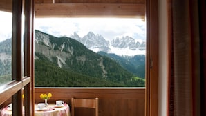 A wooden cabin with a table and chair, a vase with yellow flowers, and a view of snow-capped mountains. - Chalet in Funes Valley With Dolomites Views (Funes)