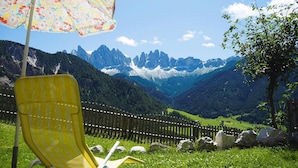 A yellow chair with a floral umbrella in a grassy area with a mountain view. - Chalet in Funes Valley With Dolomites Views (Funes)