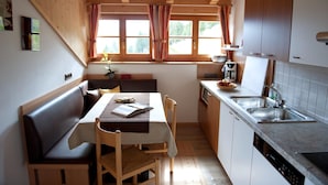 A compact kitchen with wooden cabinets, a sink, and a dining area with a bench and table. - Chalet in Funes Valley With Dolomites Views (Funes)