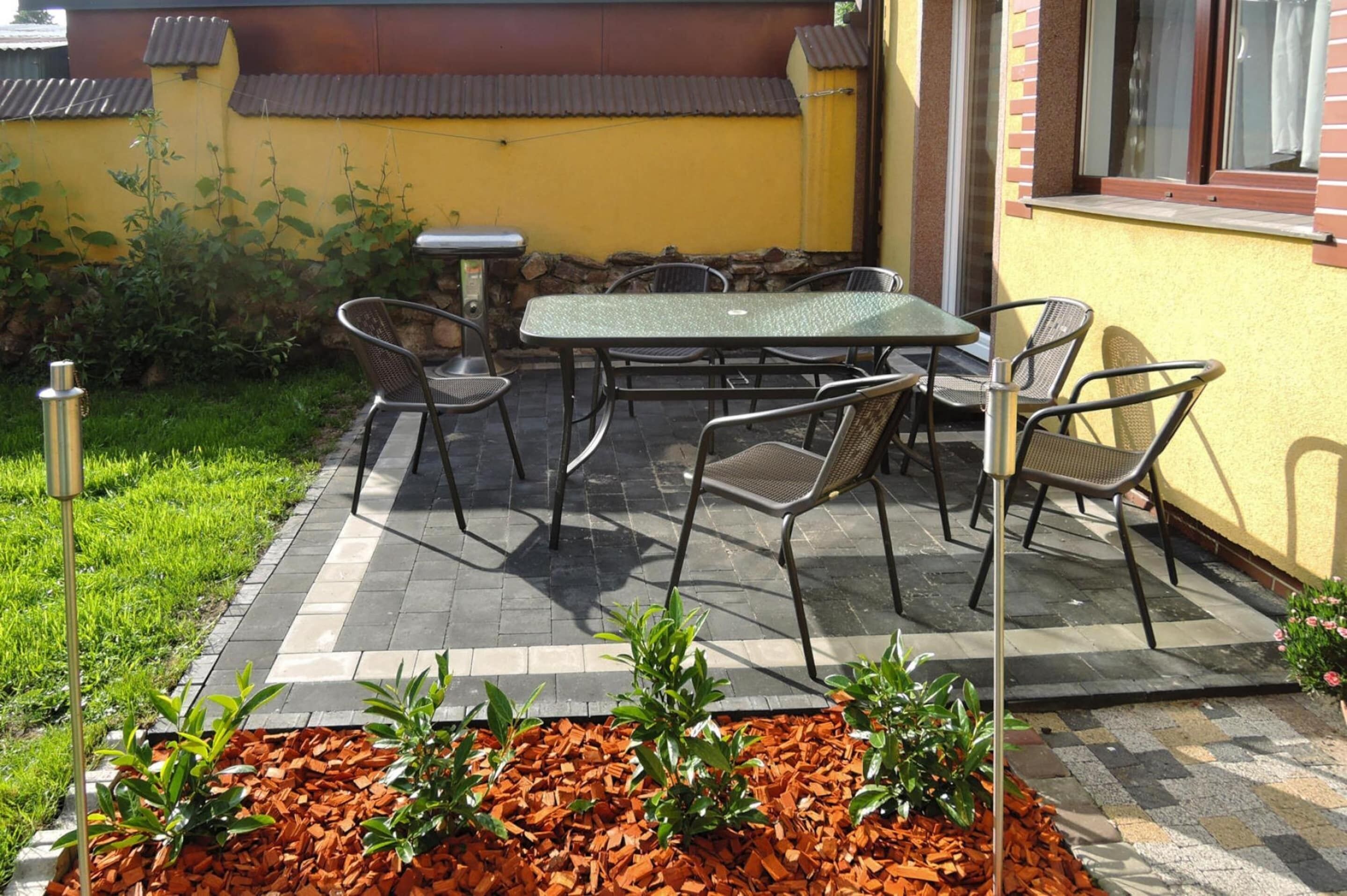Un patio al aire libre con una mesa y sillas, rodeado por un muro de piedra y un edificio amarillo.