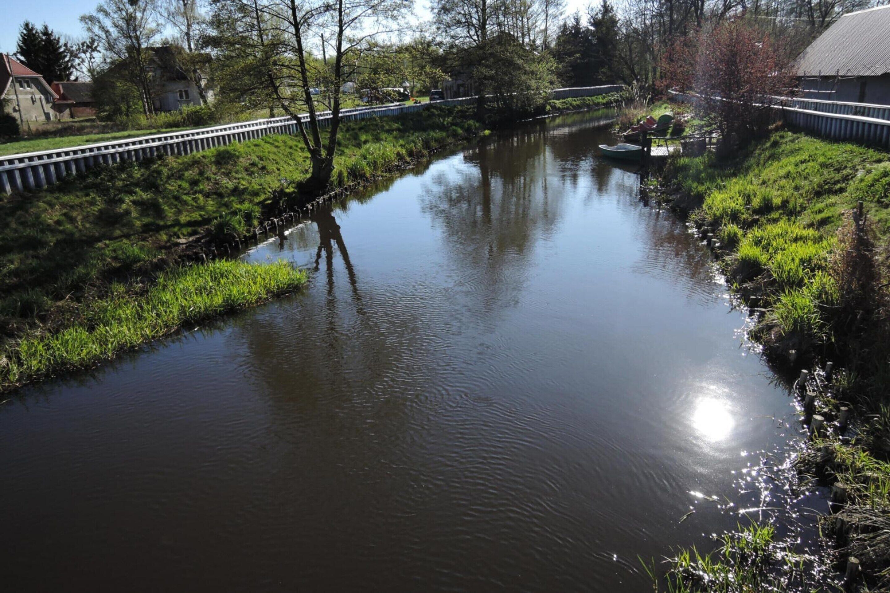 A calm river with a bridge, grassy banks, and a small boat.