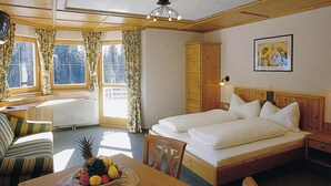 Ein Zimmer mit zwei Betten, einem Holzkopfstück, einem Nachttisch, einem Tisch mit Obst, einem Stuhl und einem Fenster mit Vorhängen.