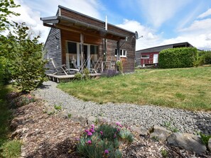 A modern log cabin with a porch, a gravel pathway, and a garden with flowers. - Holiday Home in Vulkaneifel (Berlingen)