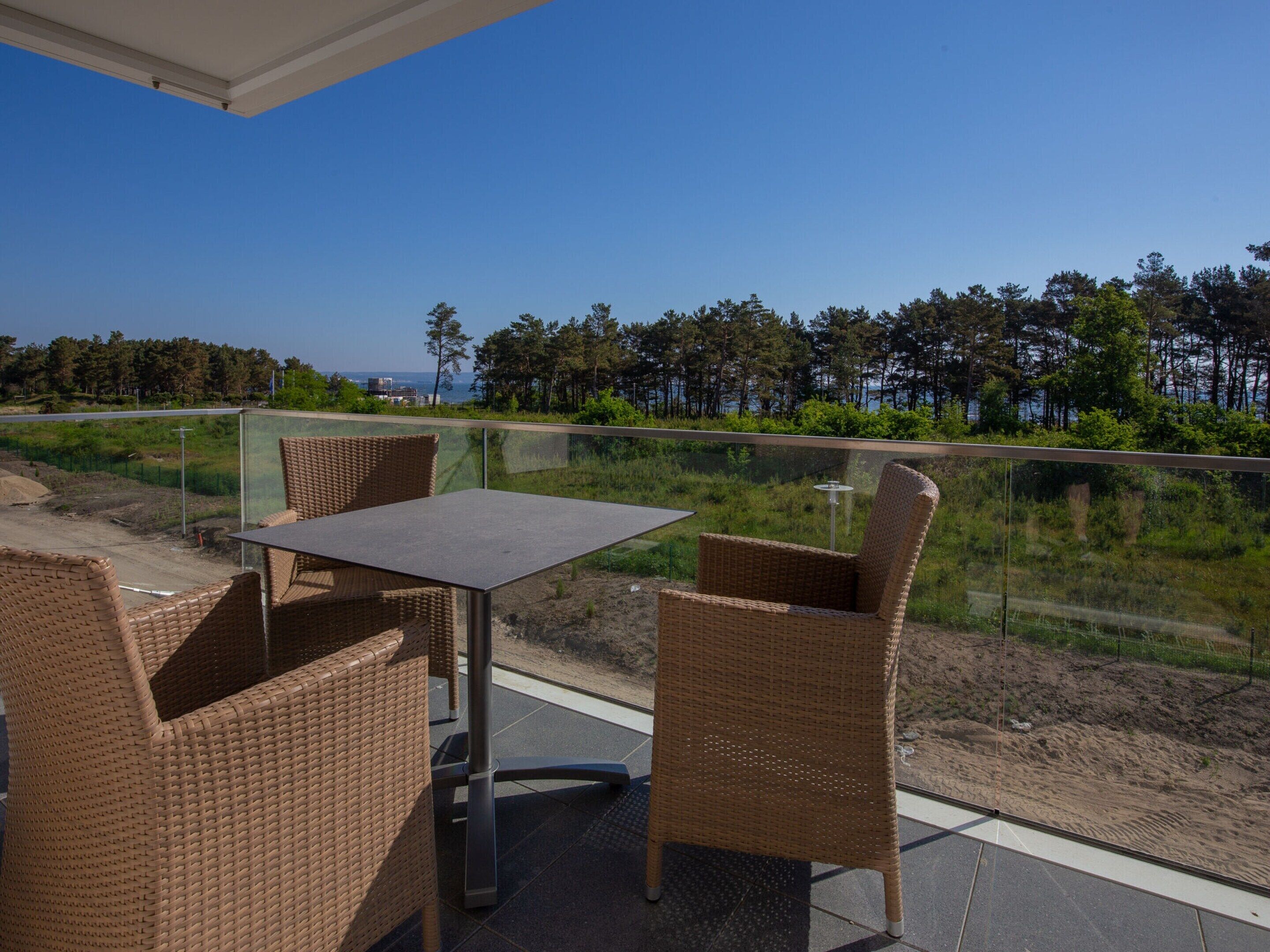 Un balcon doté de meubles en osier et d’une table, offrant une vue sur une zone boisée et un plan d’eau.