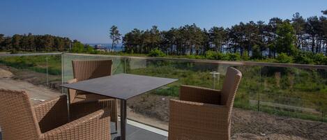 Un balcon doté de meubles en osier et d’une table, offrant une vue sur une zone boisée et un plan d’eau.