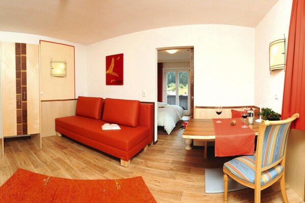 Una sala de estar moderna con un sofá rojo, una mesa de comedor con sillas y vista a un dormitorio por una puerta abierta.