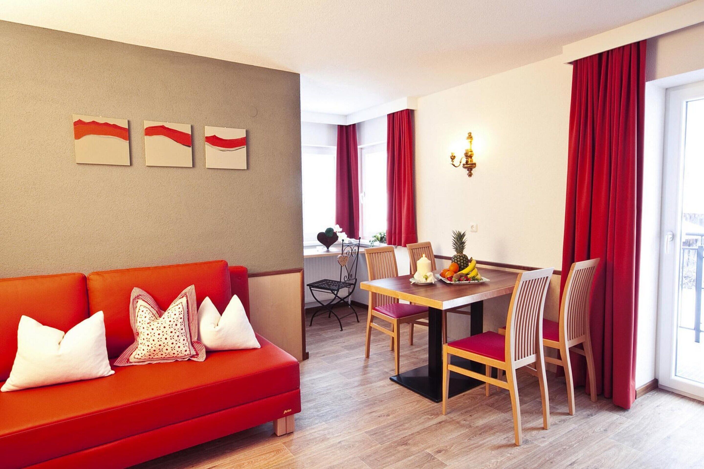 A modern living room with a red sofa, a dining table with chairs, and artwork on the wall.
