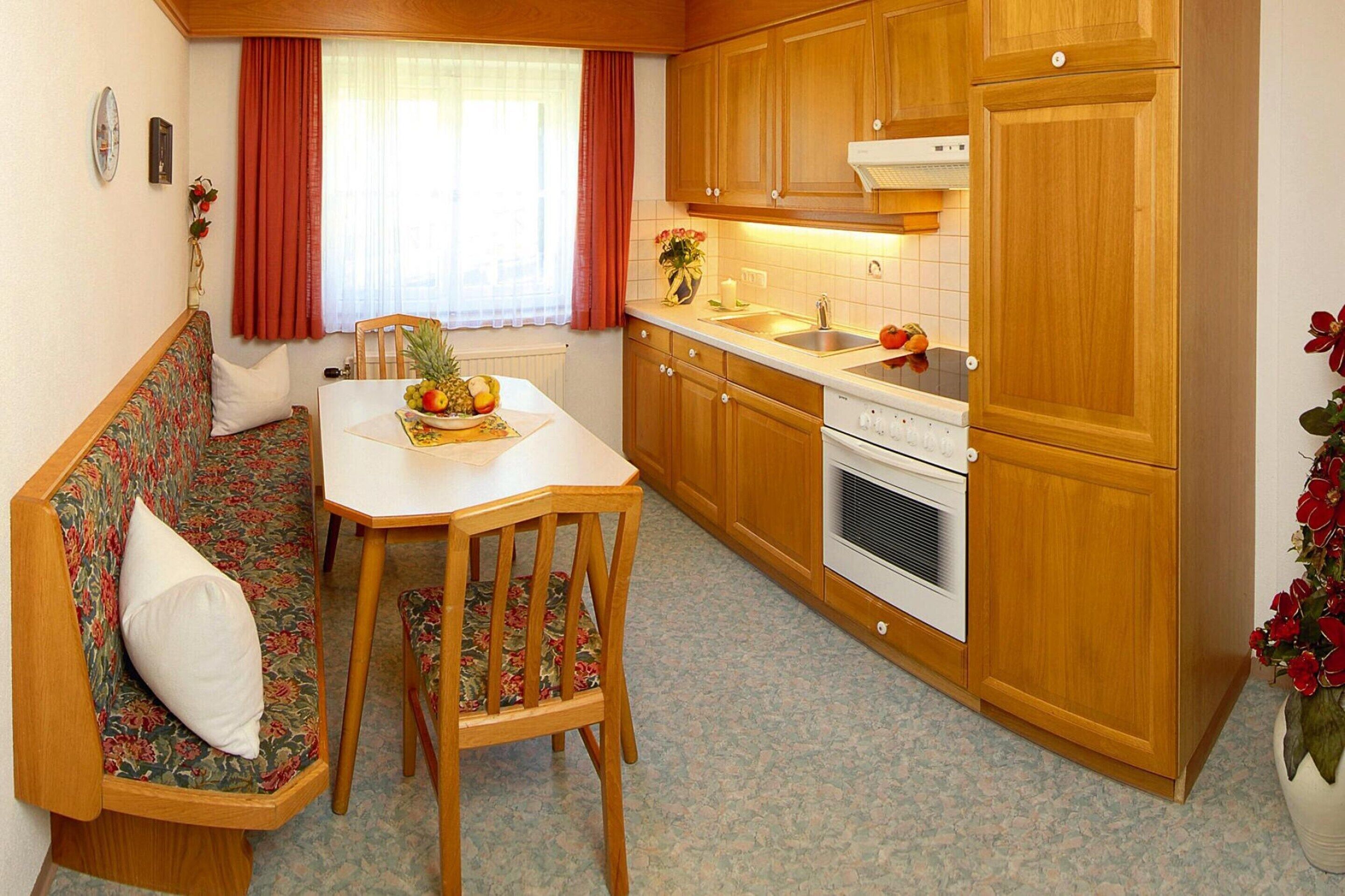 A compact kitchen with wooden cabinets, a white countertop, and a dining area with a bench and table.