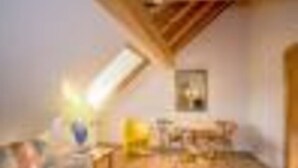 A room with a sloped ceiling, a bed, a bedside table, and a window.