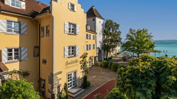 A yellow building with a sign reading "Schnitzelhaus" and a cobblestone path leading to a waterfront.