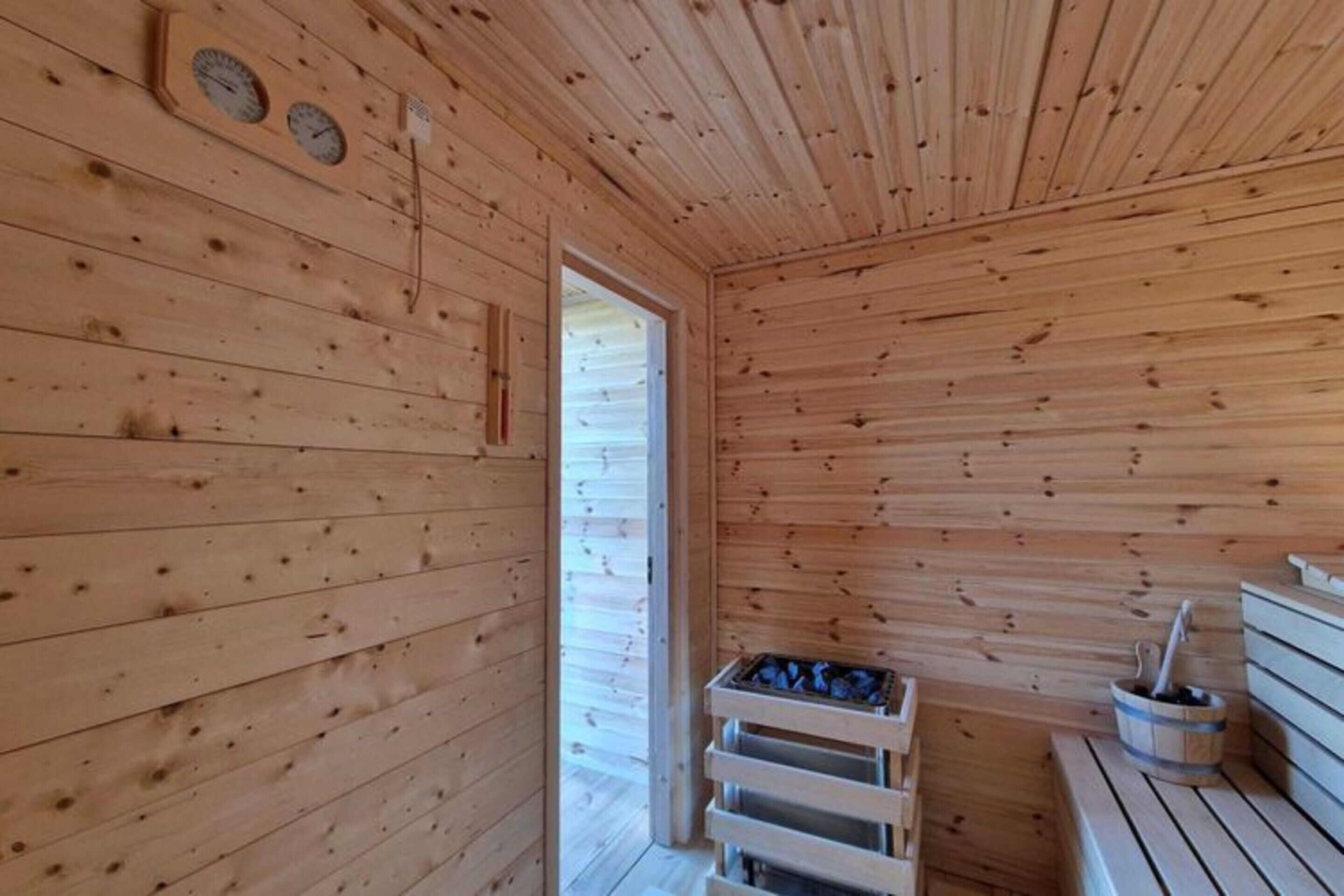 A wooden sauna room with benches, a bench with a bucket, and a door leading outside.