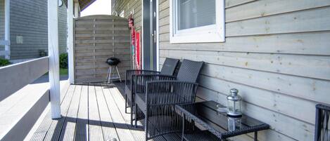 A covered outdoor seating area with a wooden deck, metal chairs, and a table with a lantern.