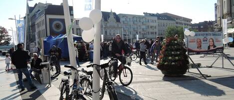 En offentlig plads med parkerede cykler, en stor blomsteropsætning og en menneskemængde.