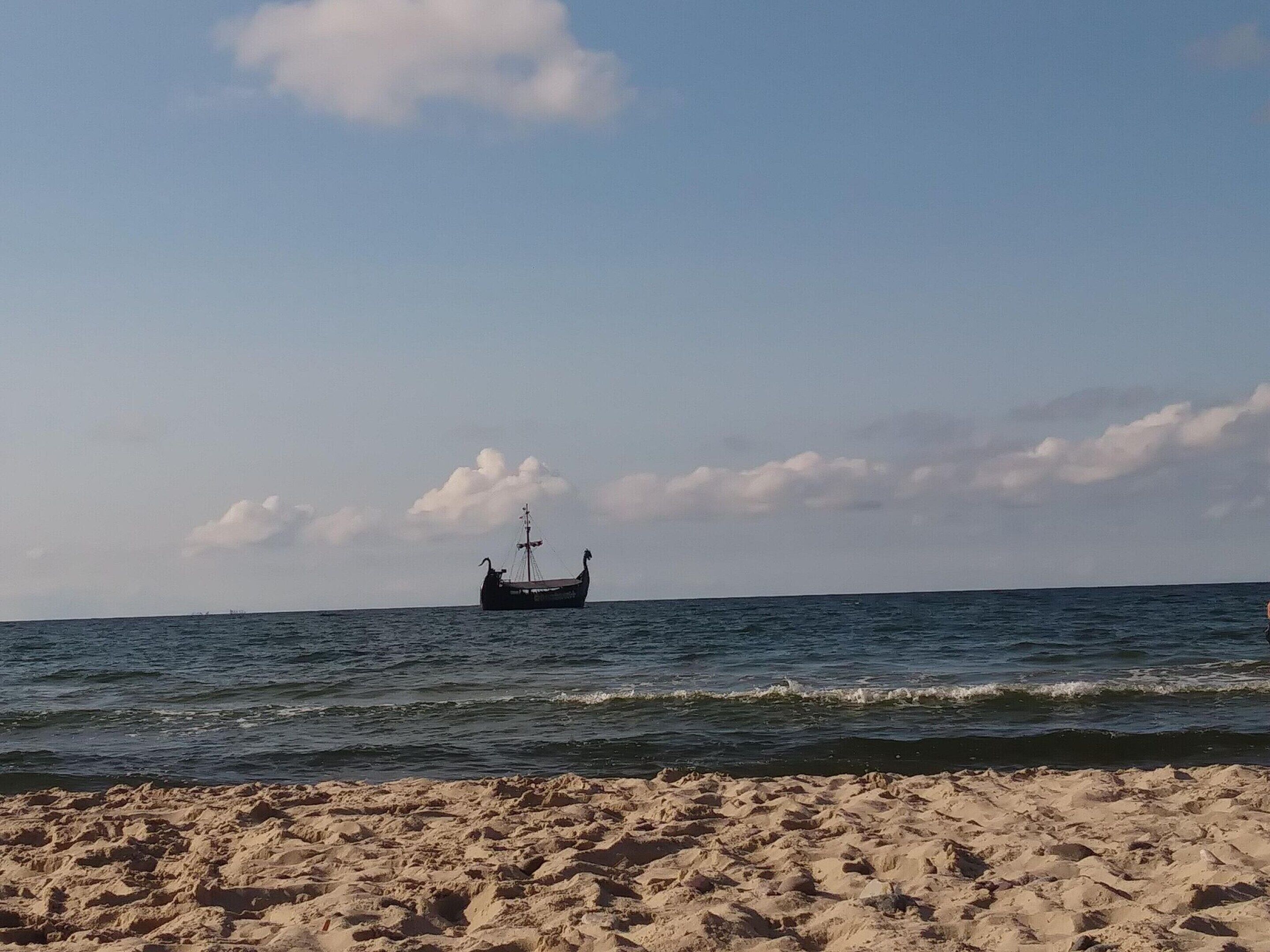Uma praia com um navio ao longe e céu claro.