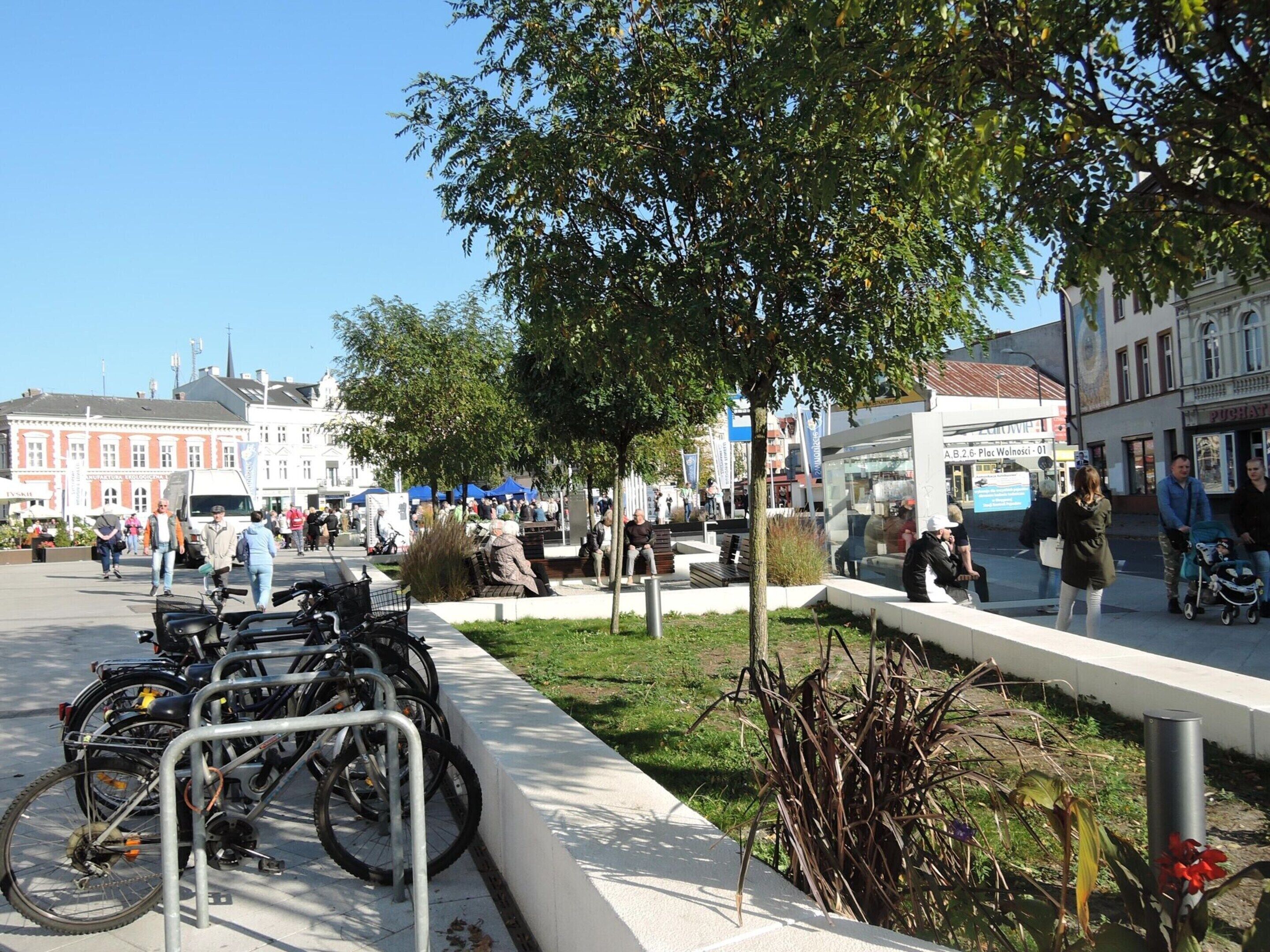 A public square with a bike parking area, benches, and a tree.